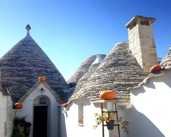 Trulli con zucche arancioni nel centro storico di Alberobello, sotto un cielo azzurro.