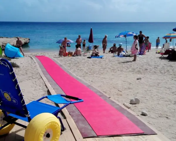 Una spiaggia attrezzata per gite per disabili, con una passerella rosa e una sedia a rotelle speciale per la sabbia.