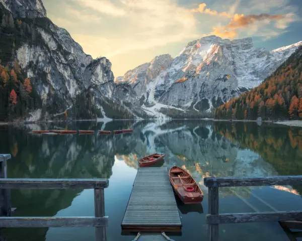 Lago di Braies, con montagne innevate e boschi autunnali riflessi sull'acqua. Per sapere come arrivare al lago di Braies in treno da Roma, cerca online.