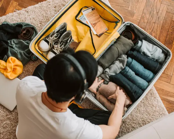 Preparazione per la gita: valigia aperta con vestiti piegati, scarpe, cintura, cappello giallo e laptop.