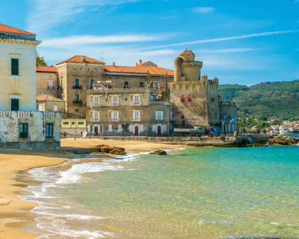 Spiaggia dorata e mare cristallino a Castellabate, con antichi palazzi e un castello che si affacciano sull'acqua. Un posto al mare da sogno.
