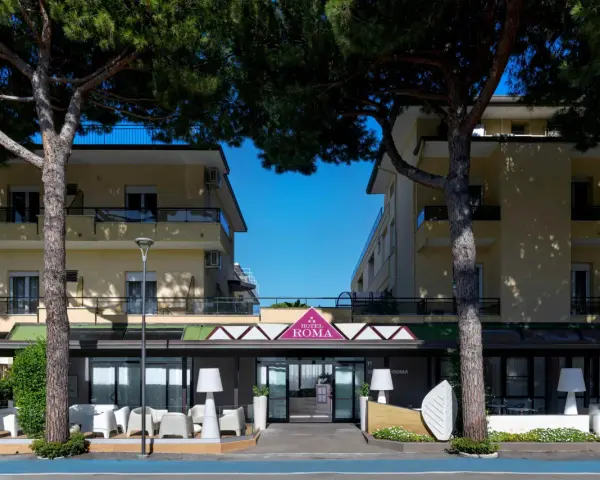 Hotel Roma Cesenatico, con pini marittimi e arredi esterni moderni, invita al relax.