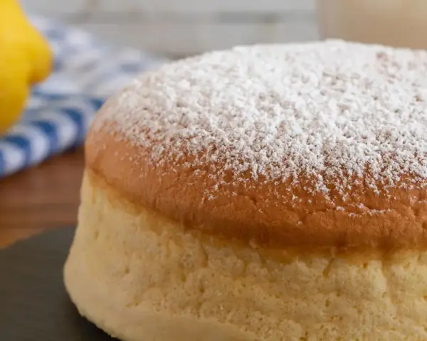 Torta al vento mantovana soffice e leggera, cosparsa di zucchero a velo. Accanto, un limone e un tovagliolo a righe blu.