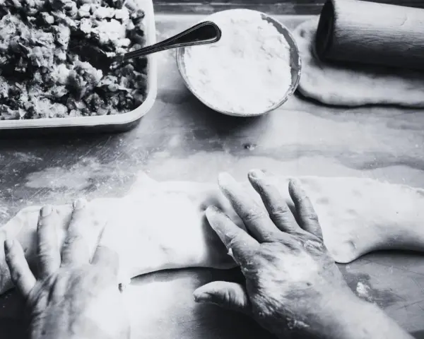 Mani esperte modellano la pasta per creare un'azdora romagnola, con ripieno e farina pronti.