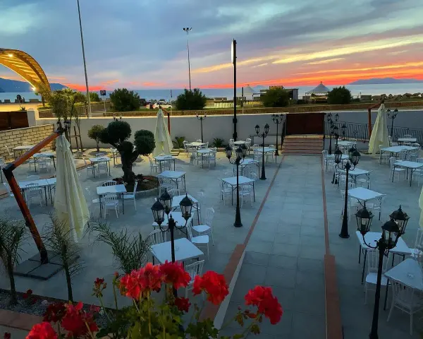 Terrazza di un ristorante al tramonto, con tavoli apparecchiati e fiori rossi. Un invito a scoprire il **vecchio palmento menu**.