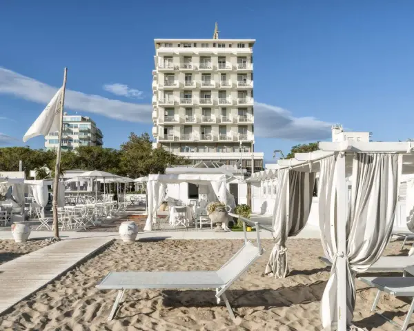 Spiaggia attrezzata con lettini e gazebo bianchi, sullo sfondo l'imponente hotel Abners.