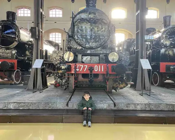 Bambino seduto davanti a un imponente treno storico al Museo di Pietrarsa, Napoli.