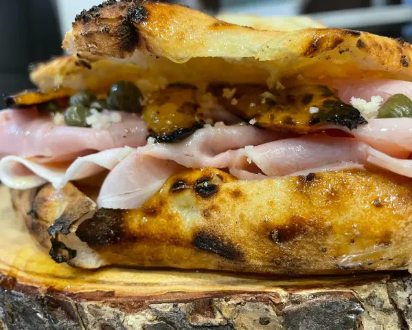 Un panino gourmet con mortadella, capperi e pomodori secchi, un vero re artù a Lecce, servito su un tagliere di legno.