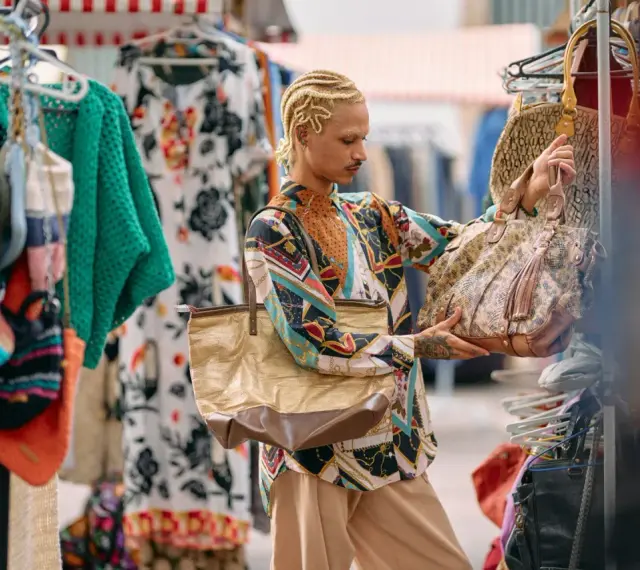 Un ragazzo con treccine bionde sceglie borse in un mercato di shopping a Roma.