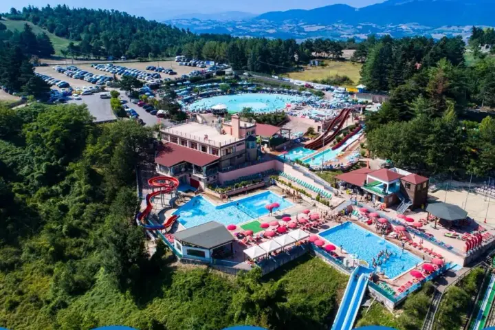 Un grande parco acquatico nelle Marche, con scivoli, piscine e tante persone che si divertono sotto il sole.