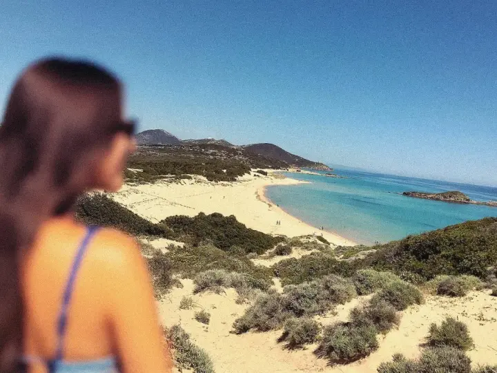 Vista mozzafiato di una spiaggia sarda, con dune sabbiose e macchia mediterranea. Perfetta per le gite in Sardegna.