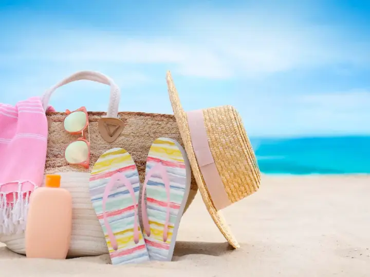 Borsa da spiaggia con asciugamano rosa, infradito colorate, occhiali da sole e cappello di paglia. Ecco cosa portare al mare per una giornata perfetta!