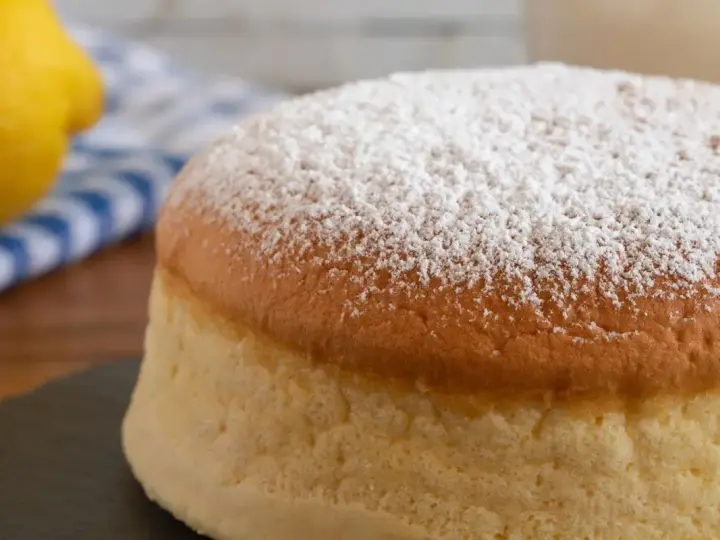 Torta al vento mantovana soffice e leggera, cosparsa di zucchero a velo. Accanto, un limone e un tovagliolo a righe blu.
