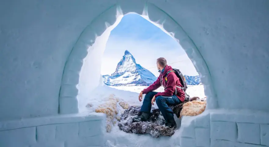 Un uomo ammira il maestoso Cervino dall'interno di un igloo, un'esperienza unica di dormire in un igloo in Italia.