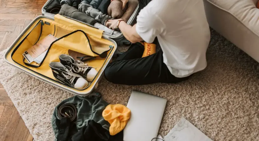 Preparazione per il viaggio: cosa si può portare in aereo. Valigia aperta con scarpe, vestiti, laptop e mappa.