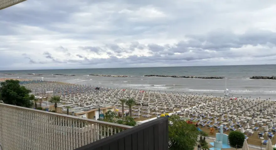 Spiaggia affollata di lettini e ombrelloni, con il mare calmo e il cielo nuvoloso. Vista dal piccadilly hotel bellaria.