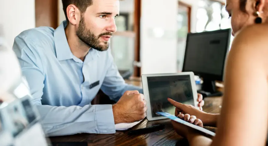 Receptionist con tablet mostra a cliente che non ci sono più camere, un caso di overbooking hotel.