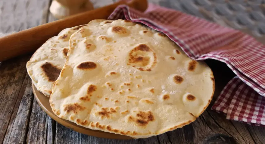 Piadine pronte per essere farcite, con un matterello e un canovaccio a quadretti. Si può fare l'impasto della piadina il giorno prima per comodità.