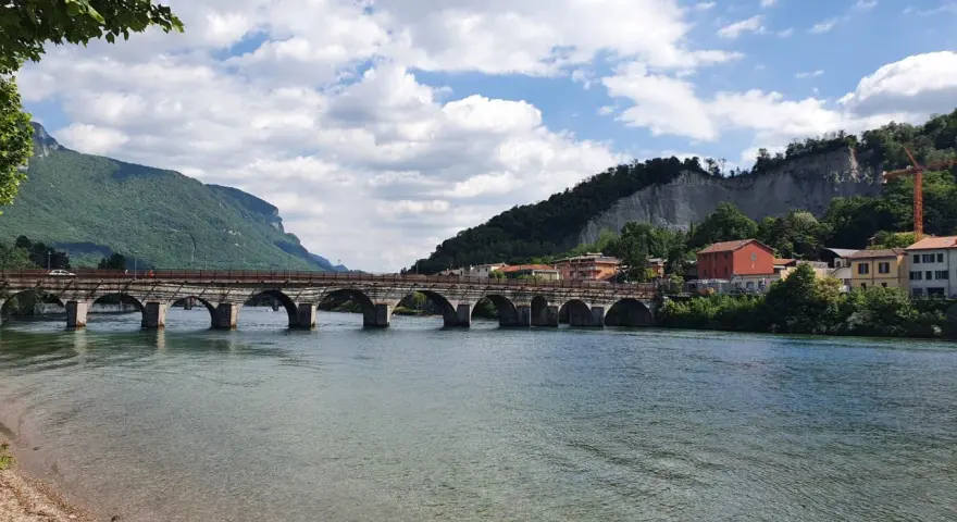 Ponte storico sul fiume Adda, con montagne verdi e case colorate. Un'ottima vista per scoprire cosa vedere a Calolziocorte.