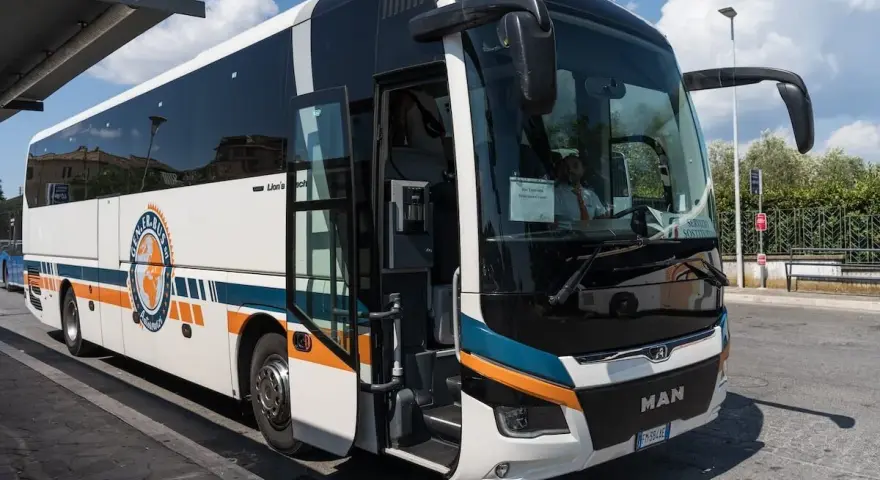 Autobus FlixBus pronto a partire da Agropoli per Roma. Il mezzo bianco con strisce arancioni e blu attende i passeggeri sotto un cielo azzurro.