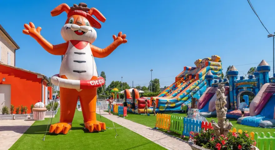 Gigante coniglio gonfiabile "Ciccio" accoglie i bambini in un parco giochi con scivoli e castelli gonfiabili, un'oasi di divertimento per gli ospiti dell'hotel Ciccio.