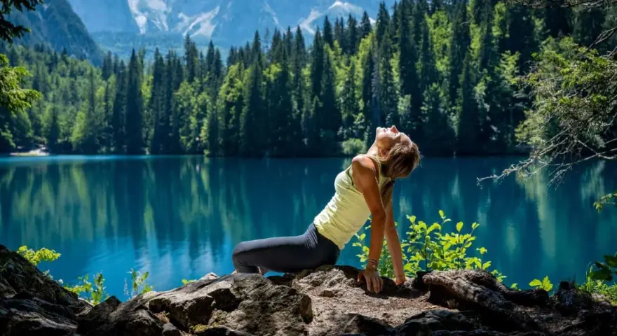 Donna in posa yoga su rocce, con lago turchese e montagne sullo sfondo. Un'immagine di serenità nella friuli montagna estate.