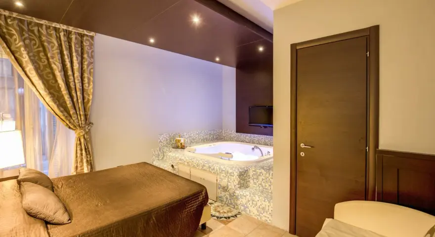 Camera con vasca idromassaggio e letto matrimoniale al **hotel The Strand**. Tende dorate e TV a parete.