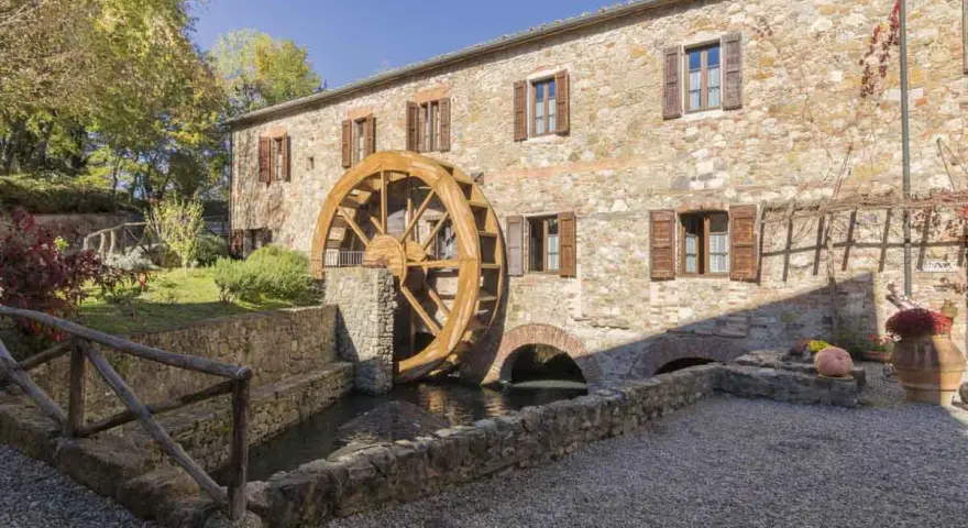 Mulino in pietra con ruota in legno, perfetto per le gite da Tuscany. Un angolo di pace tra alberi e acqua.