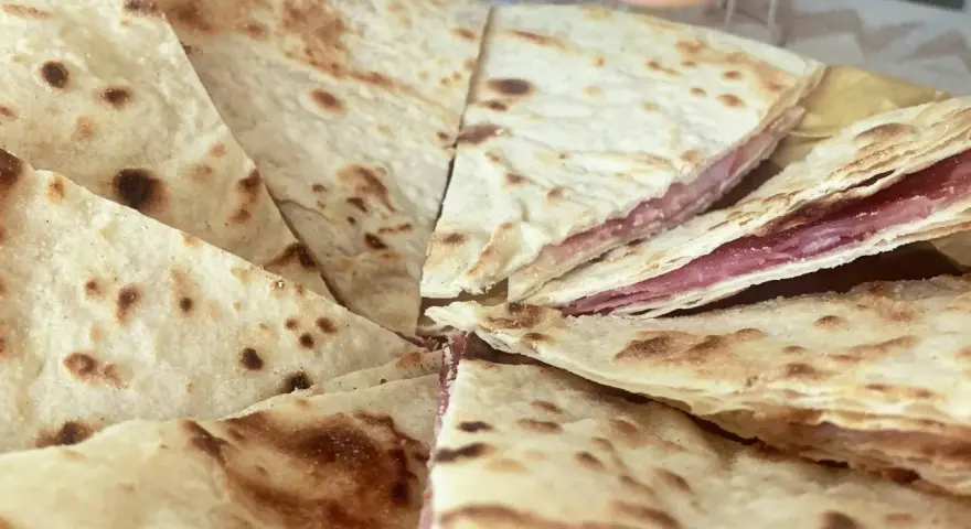 Piadina sfogliata ricetta originale, con strati sottili e ripieno di salumi, pronta per essere gustata.