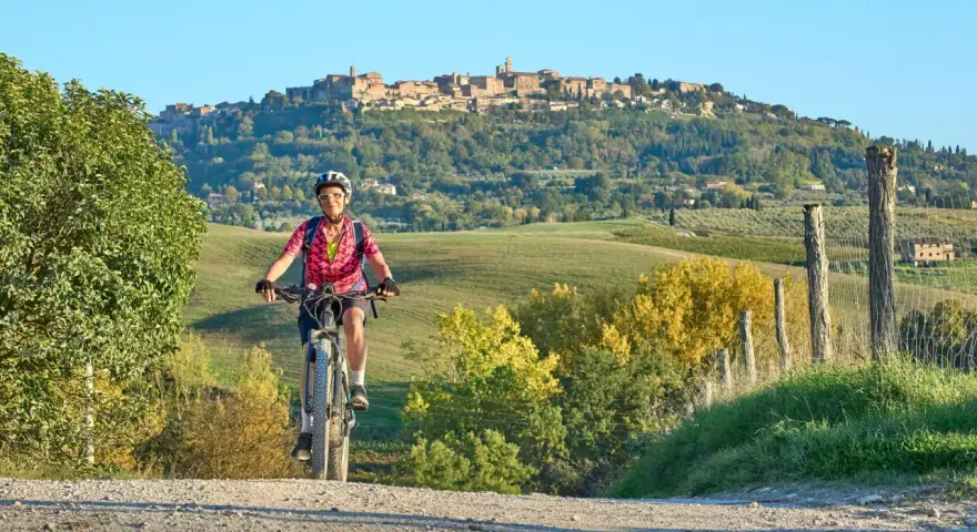 Ciclista su strada sterrata con borgo medievale sullo sfondo, un'incantevole ciclabile toscana.