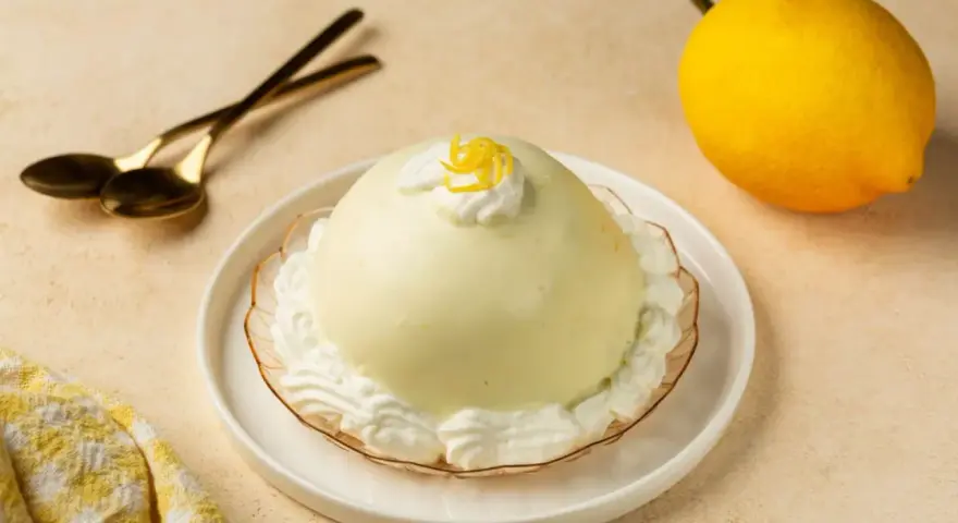 Dolce al limone, perfetto per scoprire cosa mangiare a Salerno. Servito con panna e scorzetta, pronto per essere gustato con cucchiaini dorati.