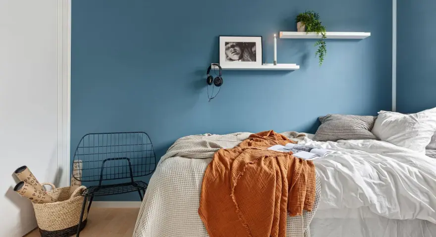 Camera da letto moderna con letto, coperta arancione, cestino e sedia in metallo. Utile per la classificazione camere hotel.