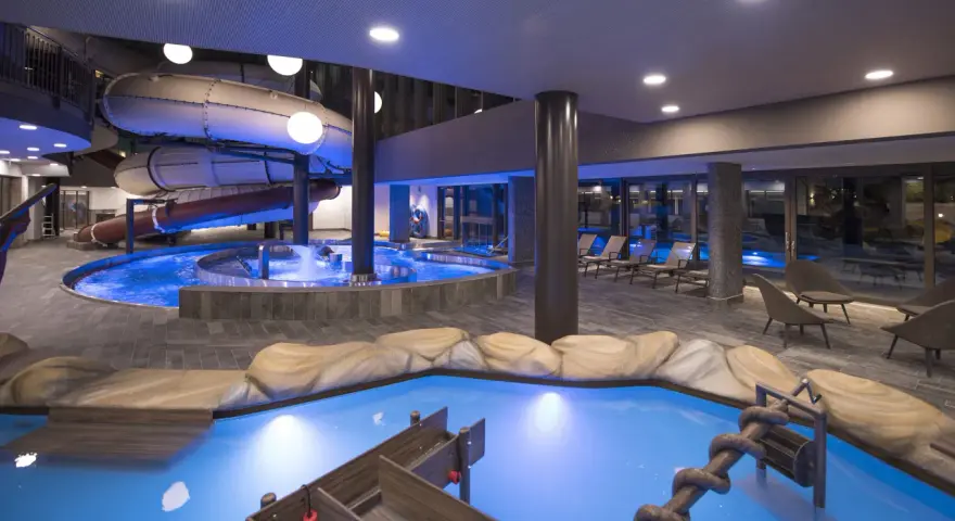 Piscina interna con scivoli acquatici e giochi d'acqua al Quellenhof Merano, un'oasi di divertimento e relax.
