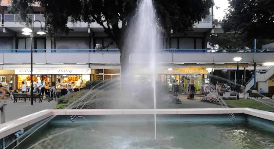 Fontana z fontanną w centrum Lido di Savio, z widokiem na sklepy i drzewa.