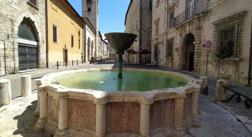 Fontana storica in pietra, un luogo incantevole tra le cose da vedere a Narni, con edifici antichi e un campanile sullo sfondo.