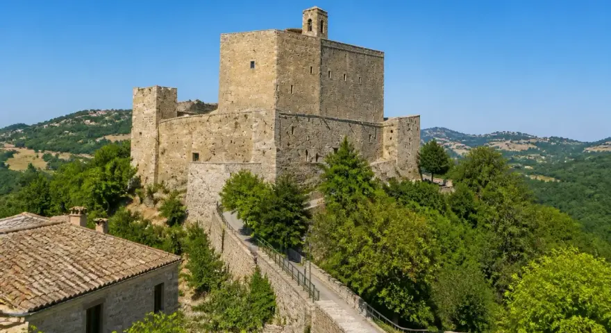 Rocche imponenti e case in pietra a Montefiore Conca, circondate da verdi colline sotto un cielo azzurro.