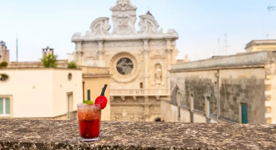 Cocktail rosso con fragola e menta, sullo sfondo la Basilica di Santa Croce. Il miglior aperitivo a Lecce.