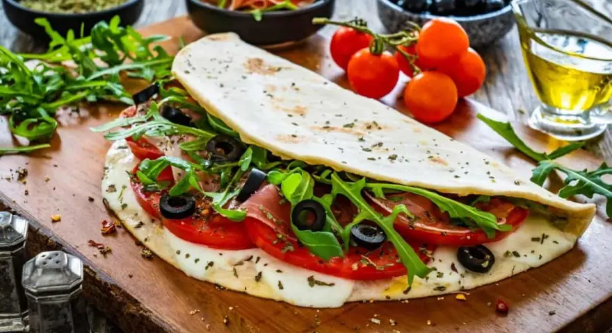 Piadina ripiena con pomodoro, mozzarella filante, rucola e olive nere. Un'esplosione di sapori per le tue farciture per piadine.