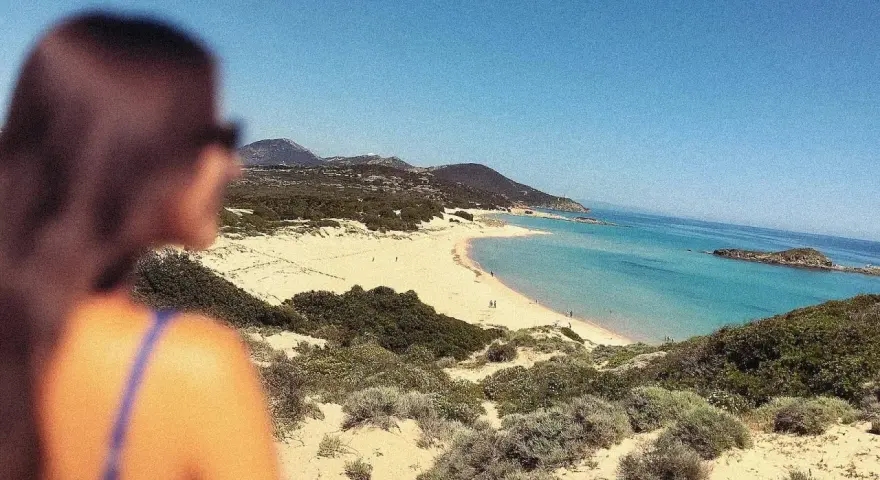 Vista mozzafiato di una spiaggia sarda, con dune sabbiose e macchia mediterranea. Perfetta per le gite in Sardegna.