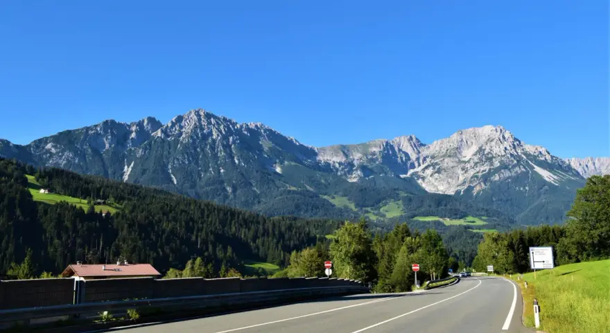 Strada panoramica per viaggi in auto in Europa dall'Italia, con montagne imponenti e boschi verdi.