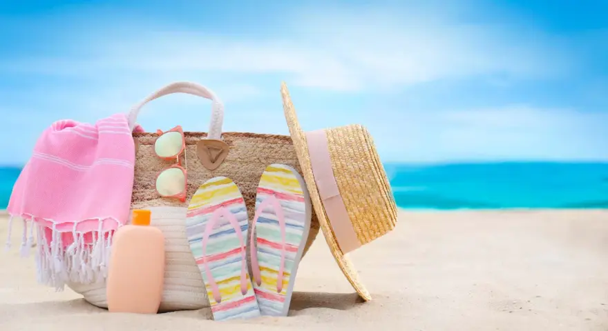 Borsa da spiaggia con asciugamano rosa, infradito colorate, occhiali da sole e cappello di paglia. Ecco cosa portare al mare per una giornata perfetta!