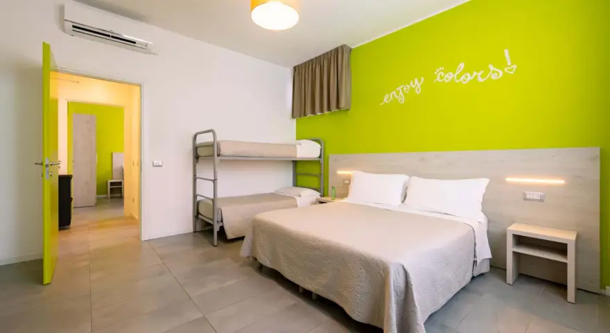 Camera luminosa con letto matrimoniale, letto a castello e parete verde brillante. Un invito a godersi i colori del green village Cesenatico.