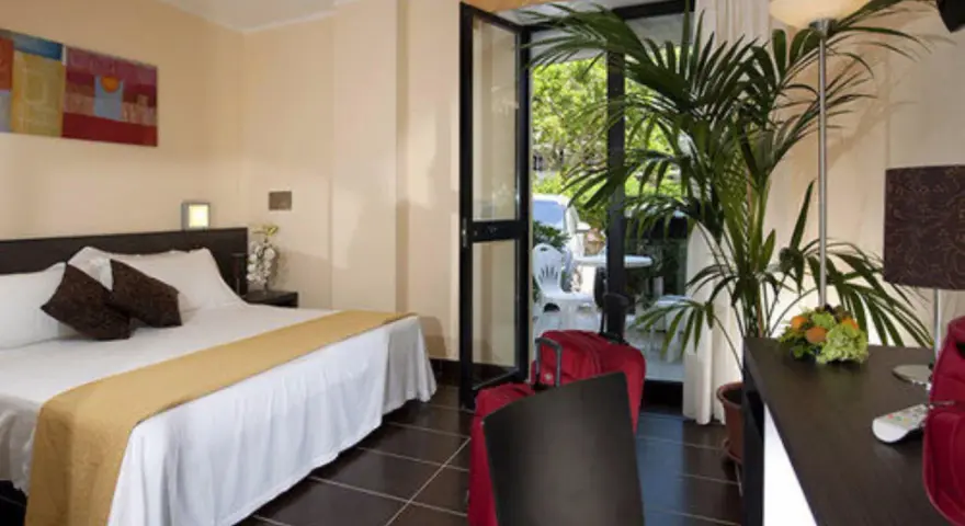 Camera accogliente al Park Hotel Kursaal Misano, con letto comodo, piante verdi e valigie rosse pronte per la partenza.