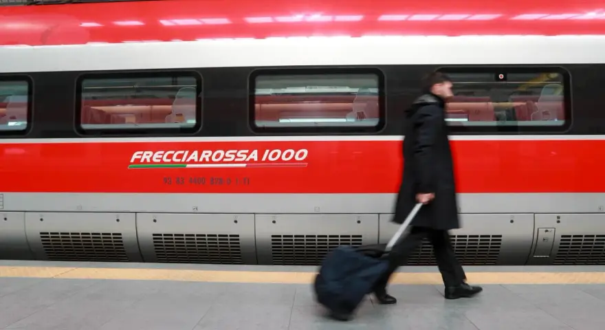 Uomo con bagagli ingombranti cammina lungo il Frecciarossa 1000.