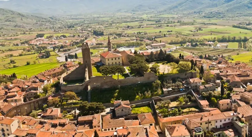 Un borgo medievale in collina, perfetto per un tour Toscana 4 giorni. Case con tetti rossi e una torre imponente dominano il paesaggio verdeggiante.