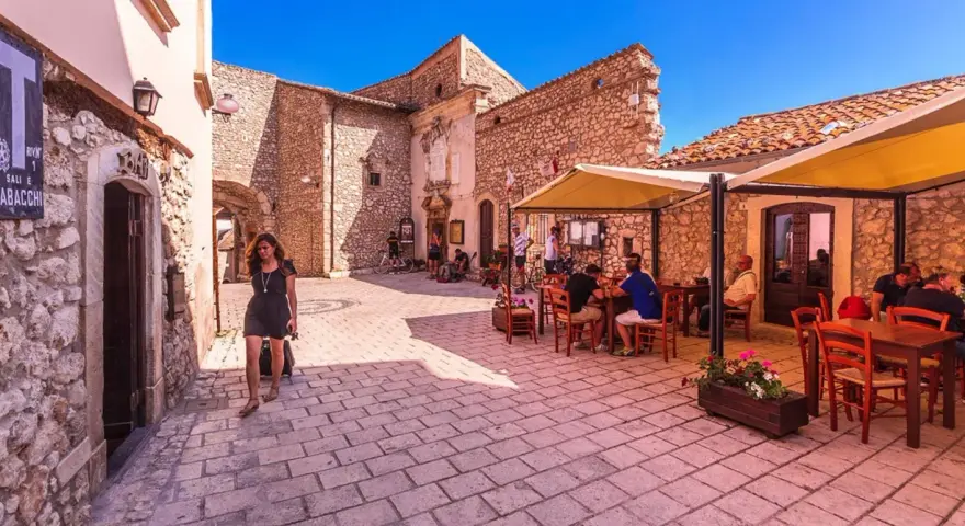 Una donna cammina in un vicolo di Santo Stefano di Sessanio, dove si trovano i migliori ristoranti. Tavoli all'aperto invitano a gustare la cucina locale.
