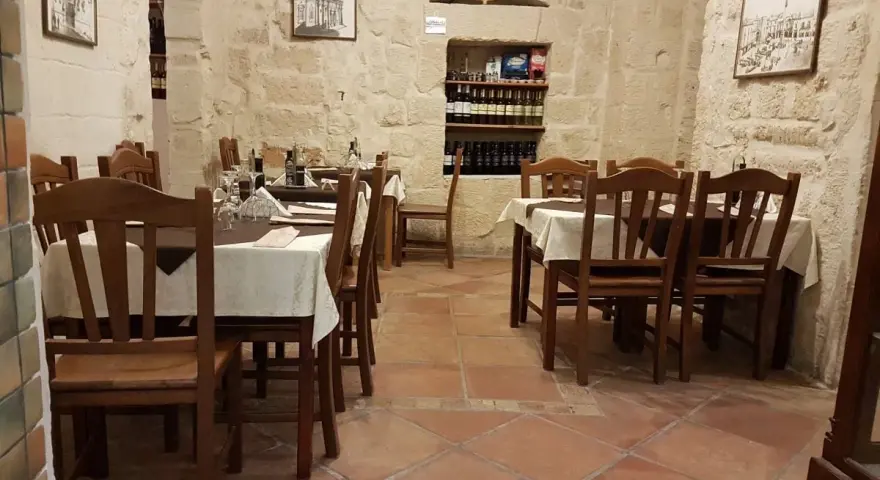 Atmosfera intima per scoprire dove cenare a Lecce: tavoli apparecchiati in pietra leccese, bottiglie di vino e quadri d'epoca.