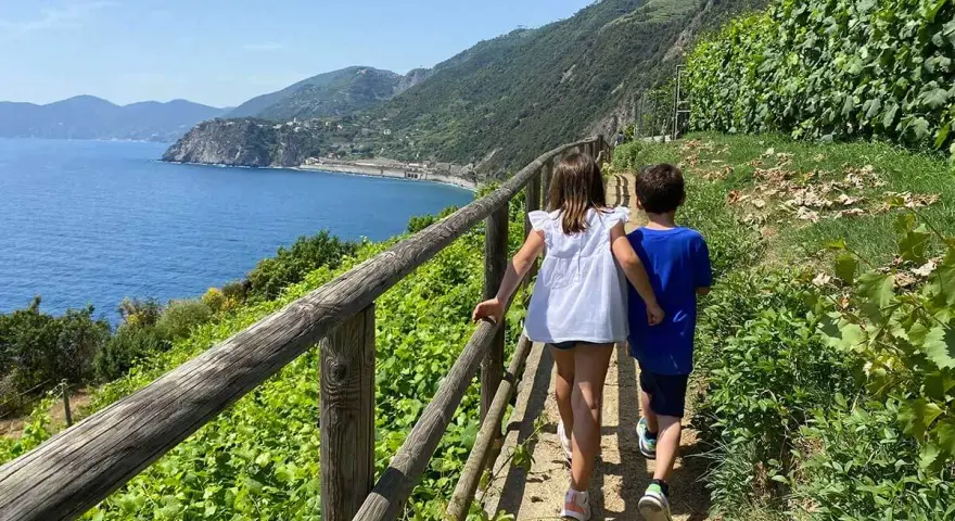 Bambini esplorano i sentieri panoramici delle Cinque Terre, con il mare blu e la vegetazione rigogliosa.