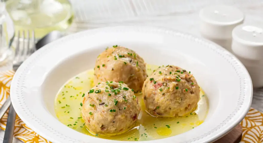 Tre canederli piatti tipici del Trentino Alto Adige, serviti in un brodo dorato e guarniti con erba cipollina.