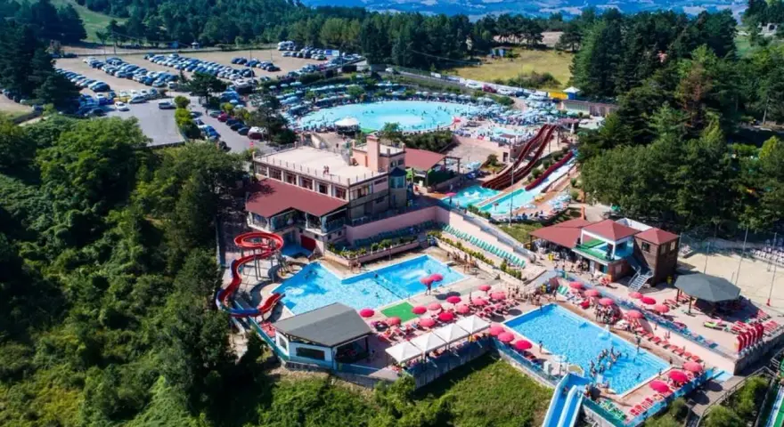 Un grande parco acquatico nelle Marche, con scivoli, piscine e tante persone che si divertono sotto il sole.